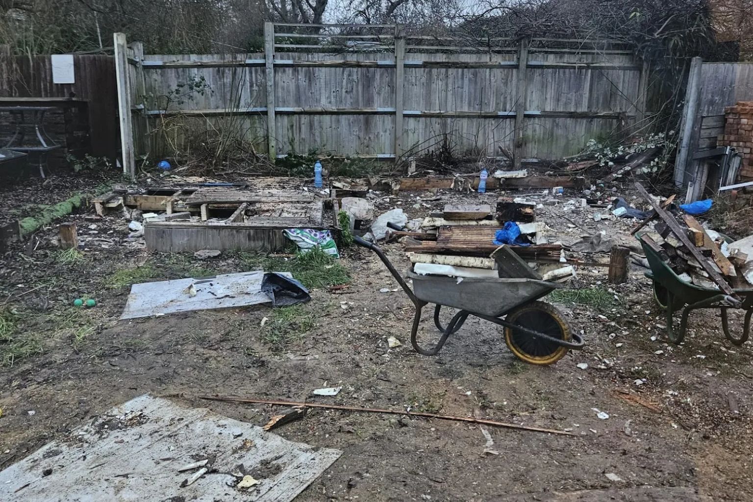 Image 1 (before): "Before photo of a heavily cluttered and excavated back garden in South East London with a wheelbarrow, scattered timber, debris, plastic sheeting, and bare compacted soil