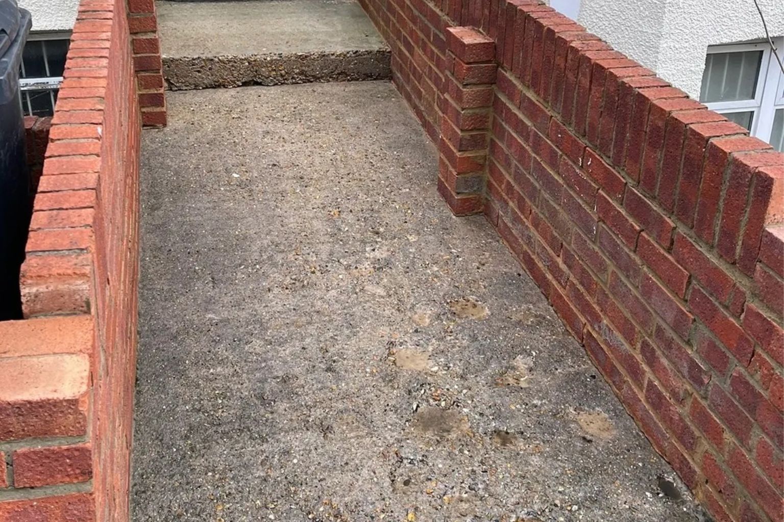 After photo of a narrow concrete pathway between two brick walls in South East London, after jet washing service by Urban Gardeners.
