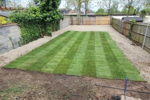 After photo of a transformed back garden featuring a neatly striped freshly laid lawn surrounded by gravel borders and wooden panel fencing