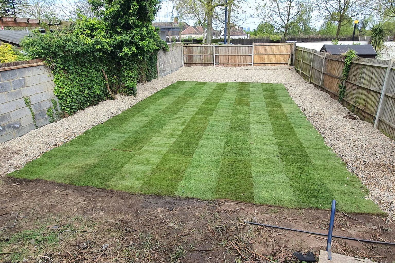 After photo of a transformed back garden featuring a neatly striped freshly laid lawn surrounded by gravel borders and wooden panel fencing